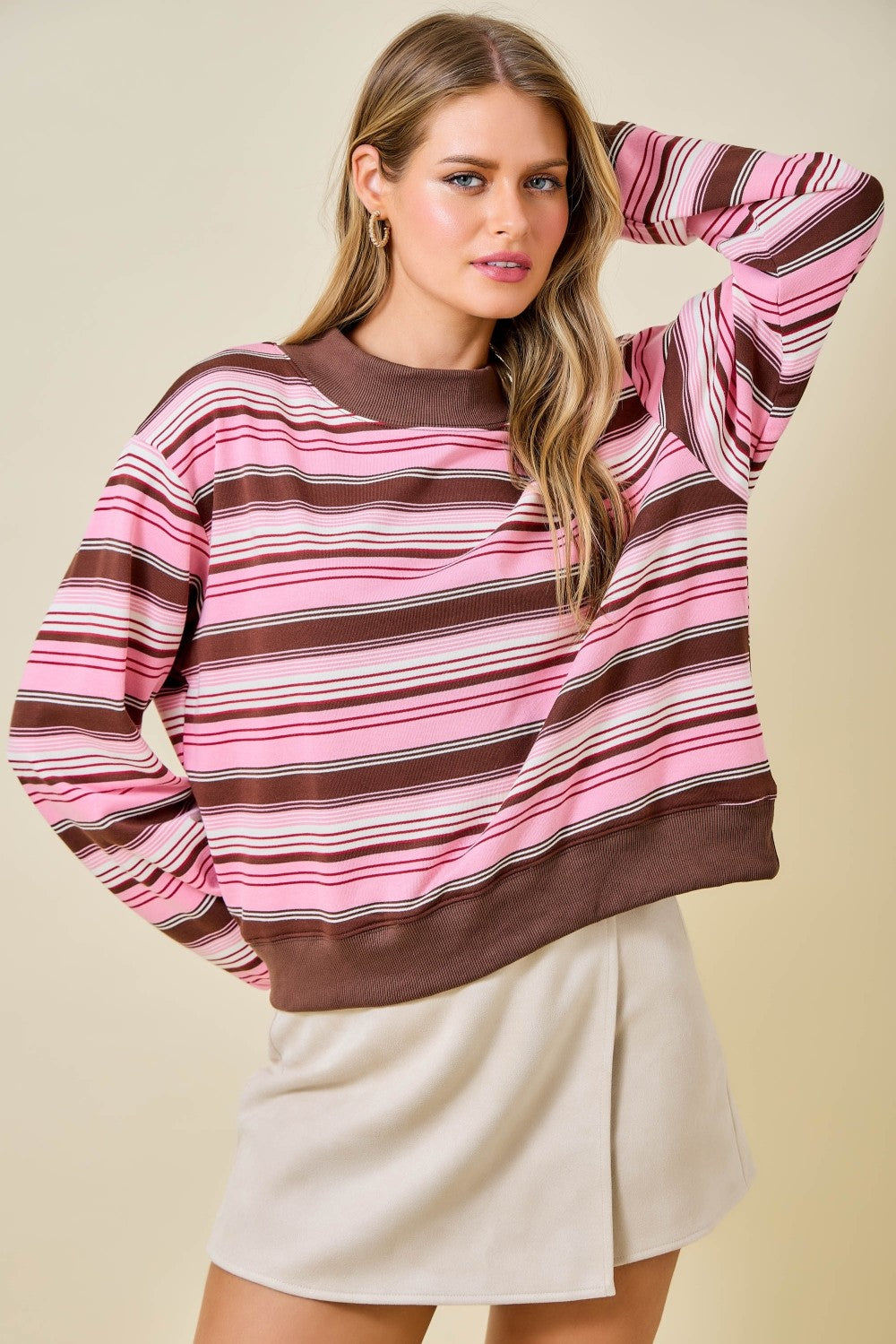 Woman wearing a pink and brown striped sweater with a beige background