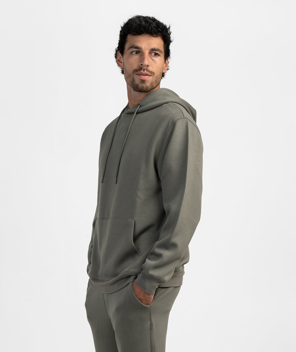 A man wearing a matching gray hoodie and sweatpants set, shown from a side profile against a clean light gray studio background.