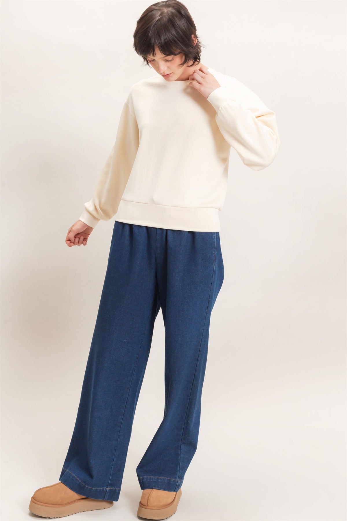 Person wearing a cream sweater and blue pants on a white background