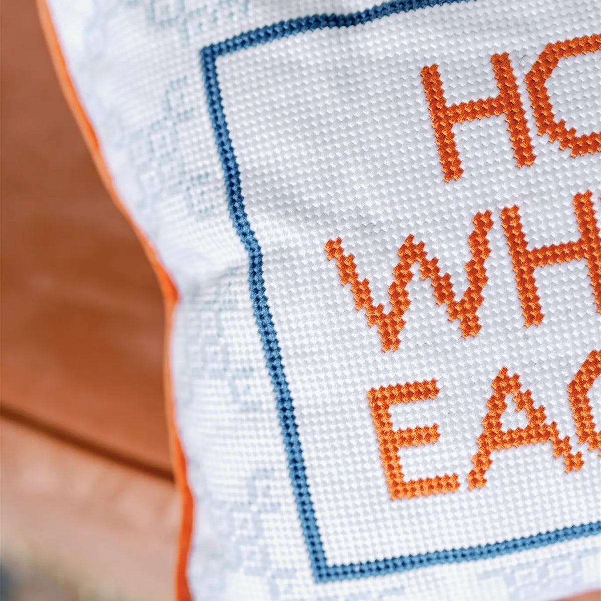 Cross-stitched text on fabric with orange letters and blue border