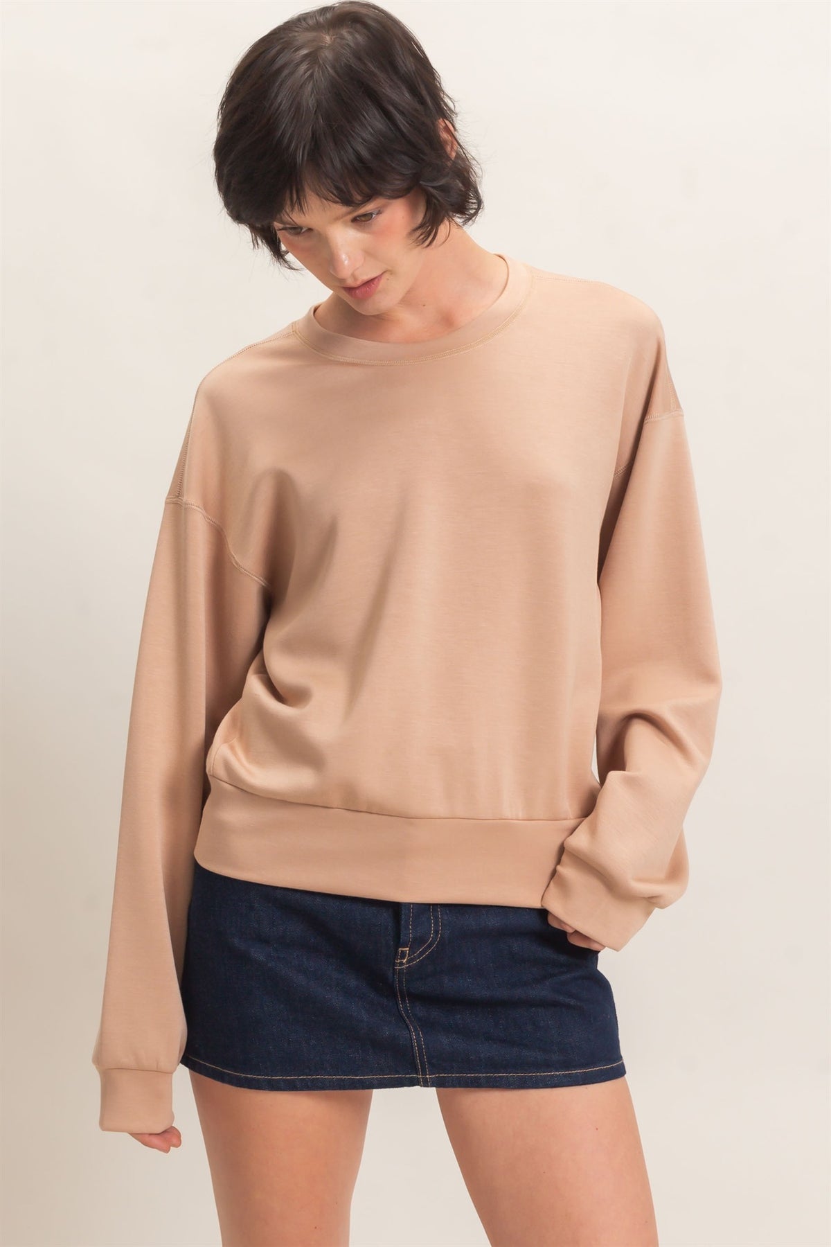 Person wearing a beige sweatshirt and dark denim skirt on a plain background