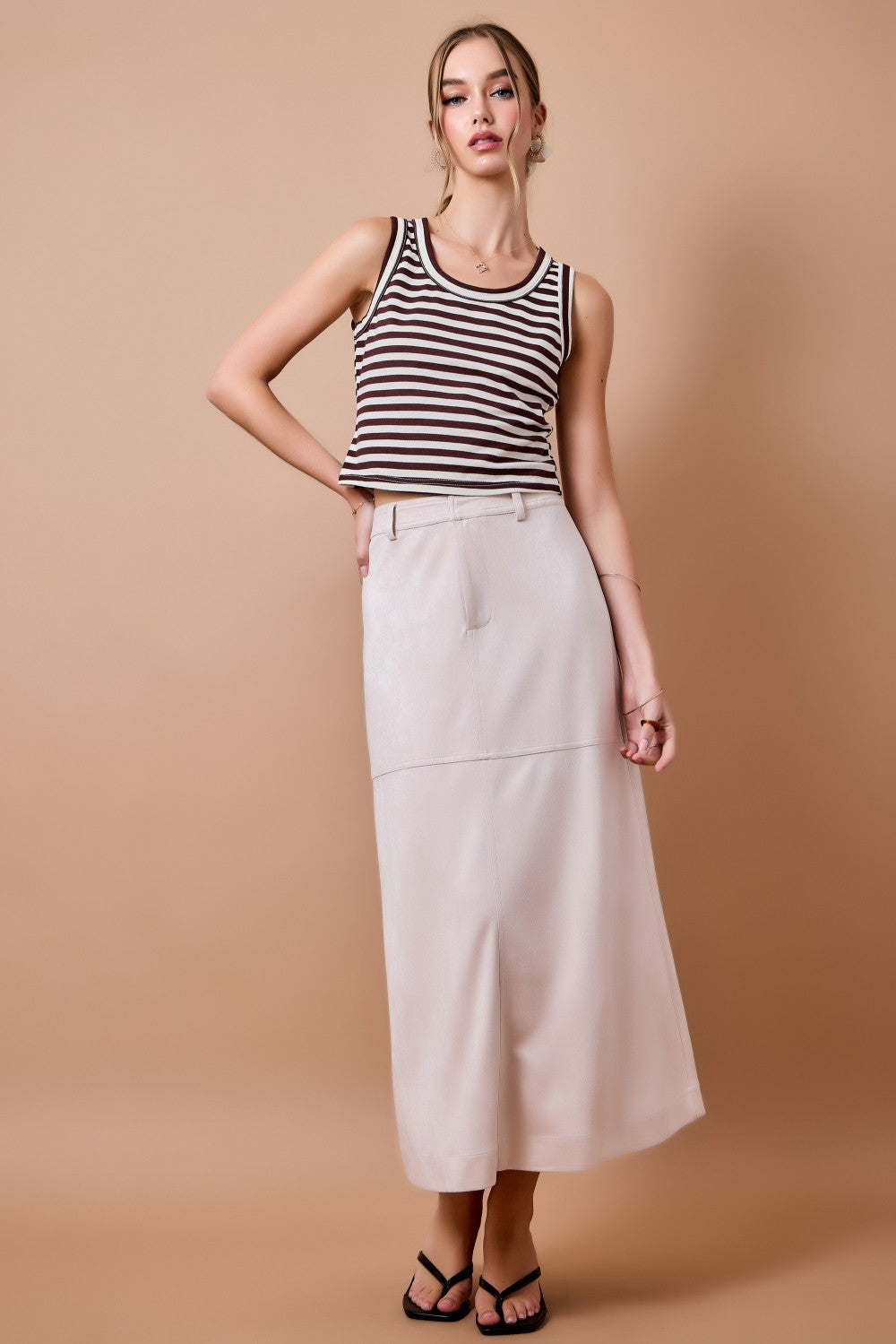 woman standing on tan background wearing cream suede skirt
