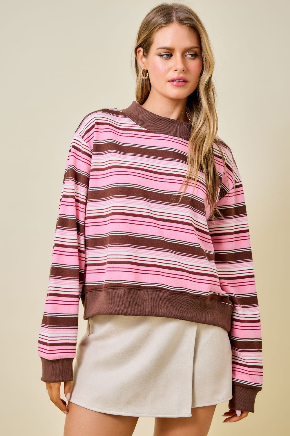 Woman wearing a pink and brown striped sweater with a beige background