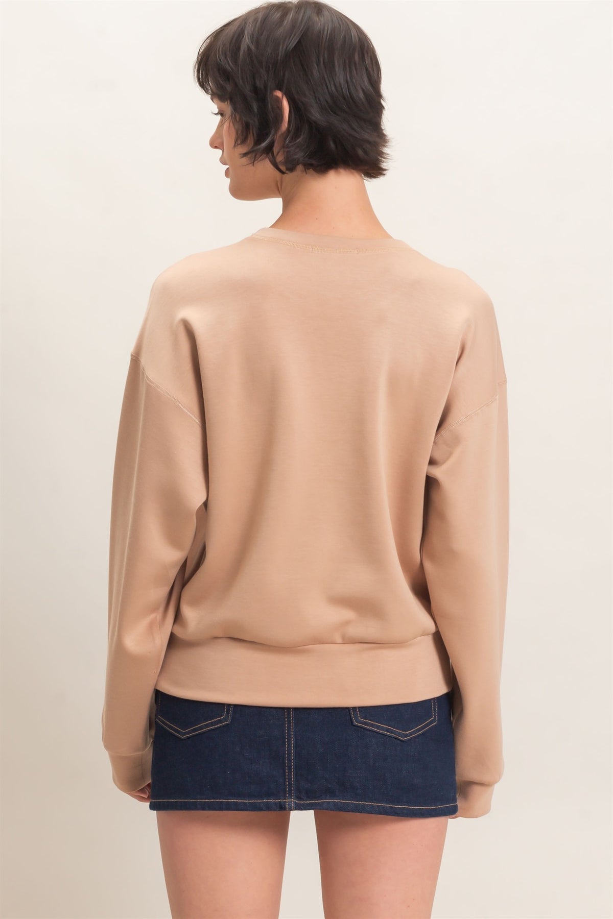Person wearing a beige sweater and denim skirt on a plain background