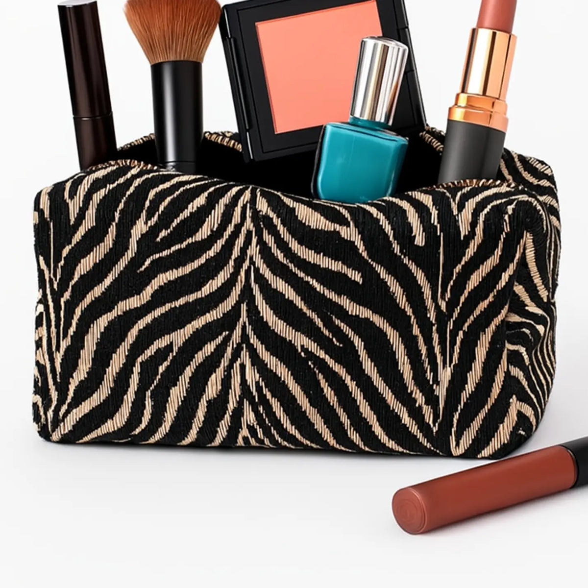 A black and beige zebra-print cosmetic bag filled with makeup items, including a brush, compact, nail polish, lipstick, and a blush, on a white background.
