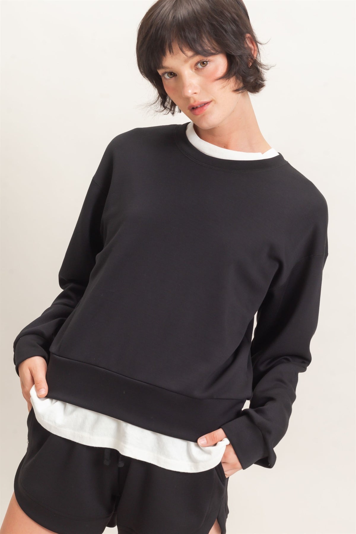 Person wearing a black sweatshirt and shorts on a plain background
