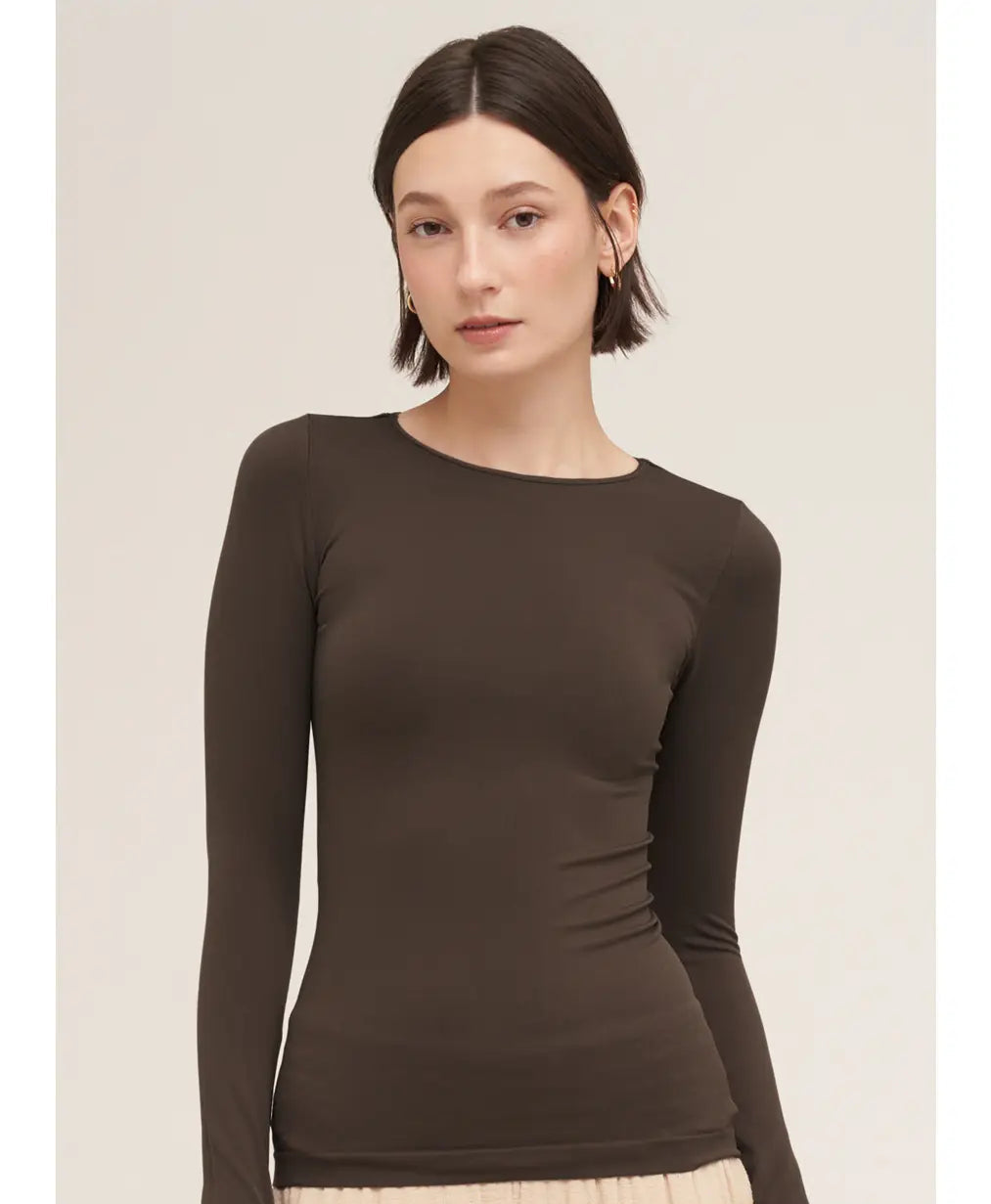 A woman modeling a fitted long-sleeve crew-neck top in dark chocolate brown, paired with a light beige skirt. 
