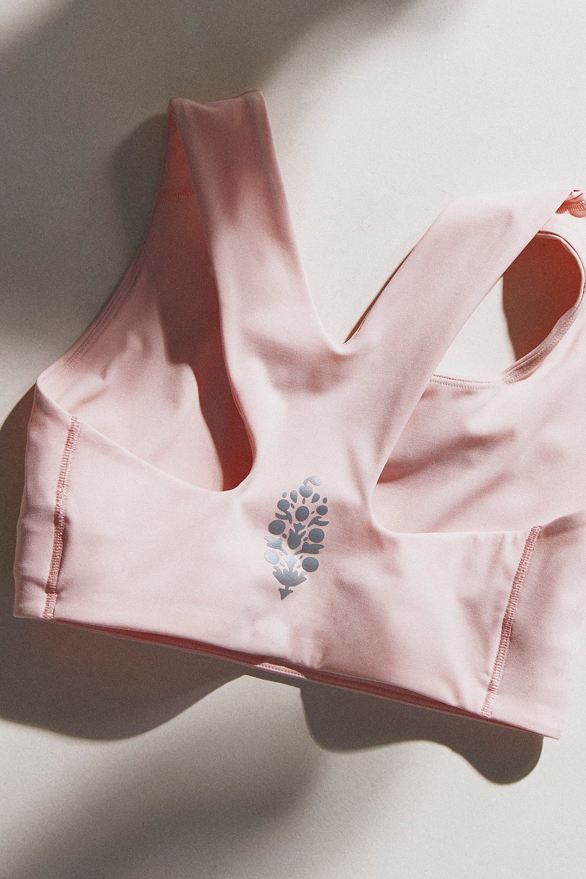 A light pink sports bra with a floral graphic on the front, laid flat on a neutral background with soft shadows.