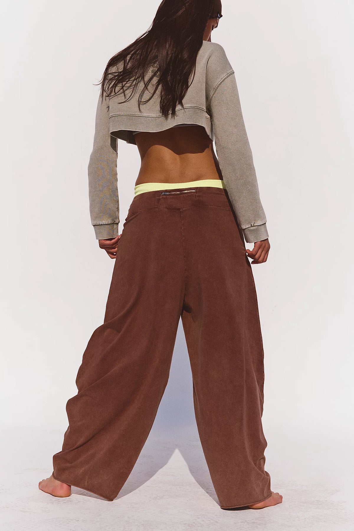 Person wearing a gray cropped top and brown wide-leg pants on a white background