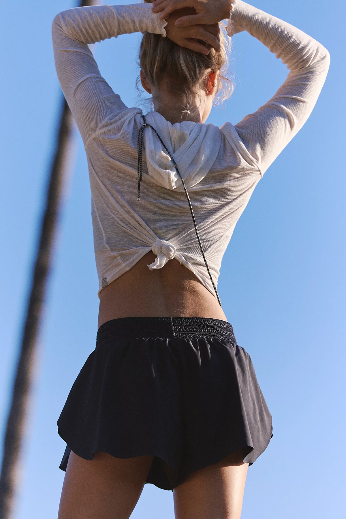 Person wearing a light gray long-sleeve top and black shorts against a clear blue sky.