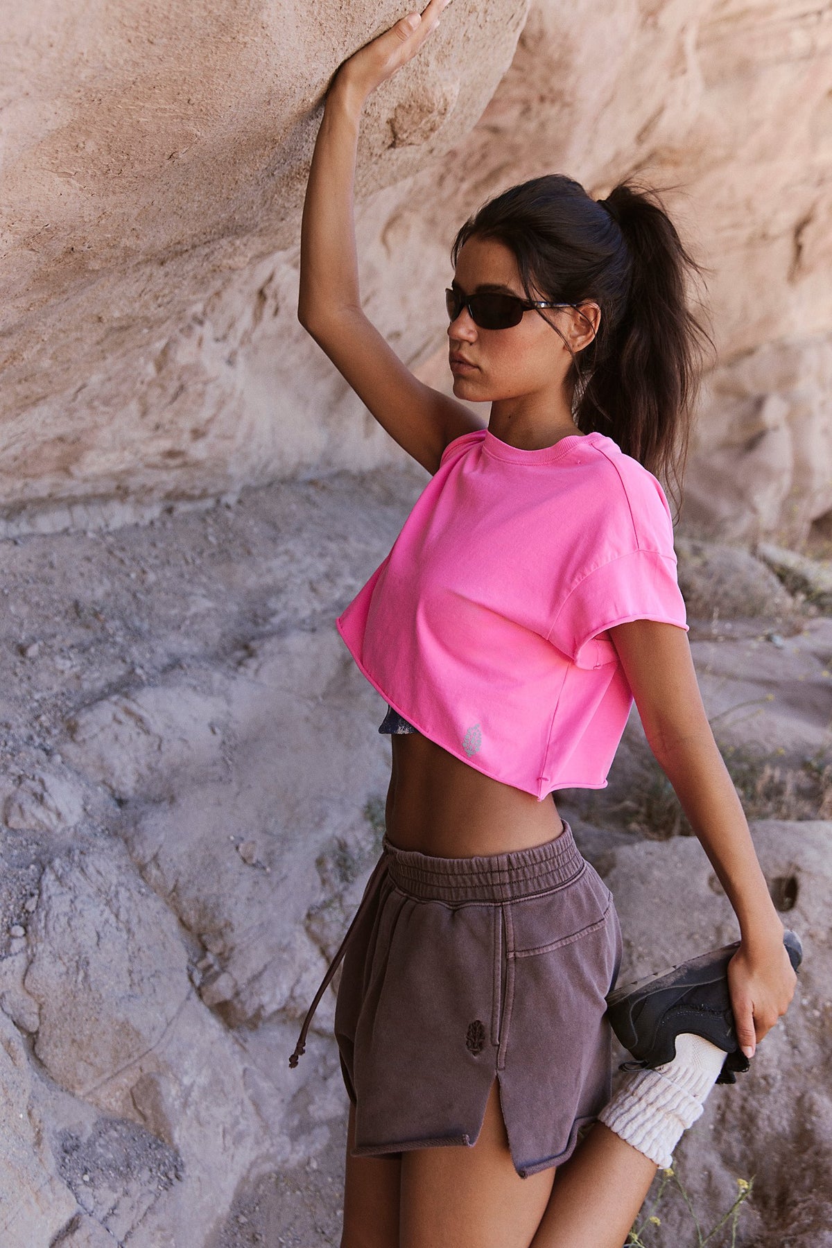 Woman in pink top and brown shorts posing against a stone wall.