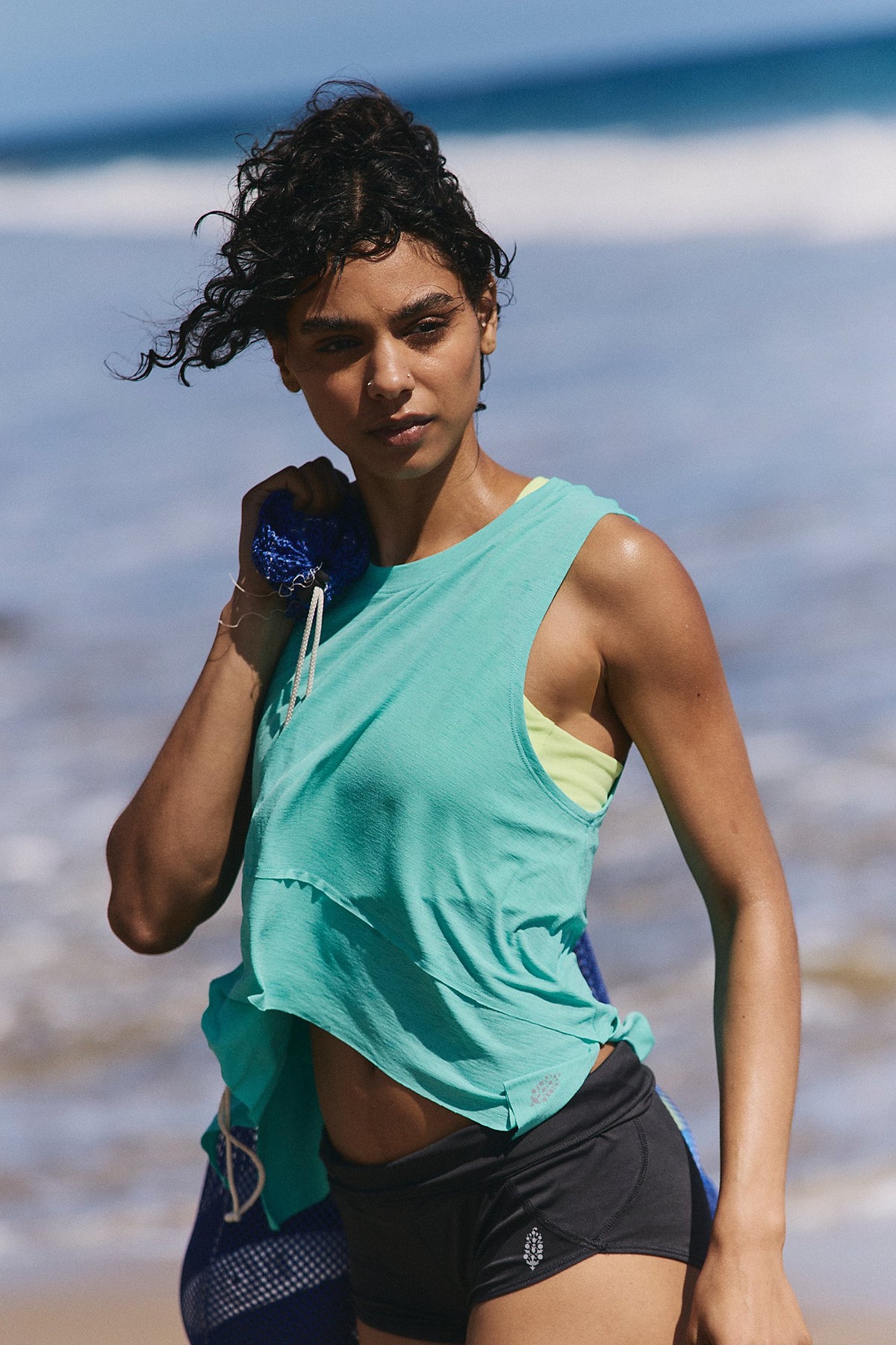 Woman in a green top and black shorts standing on a beach.