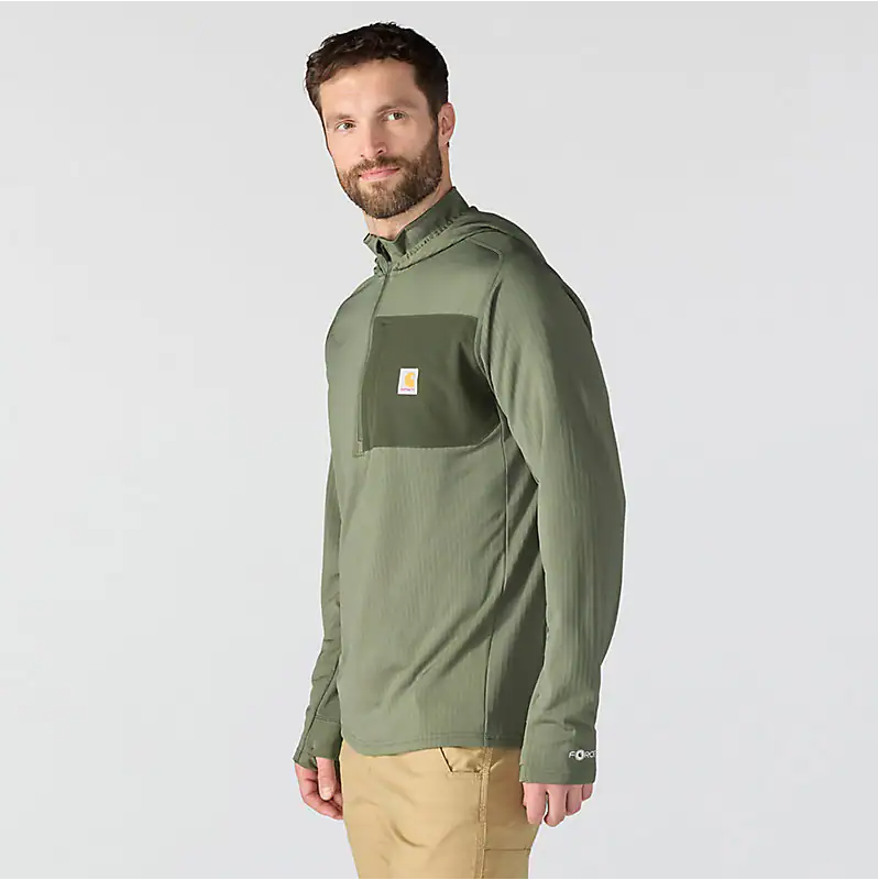 A man wearing an olive green long-sleeve quarter-zip pullover with a chest pocket and a small Carhartt logo, paired with khaki pants, against a light gray studio background.