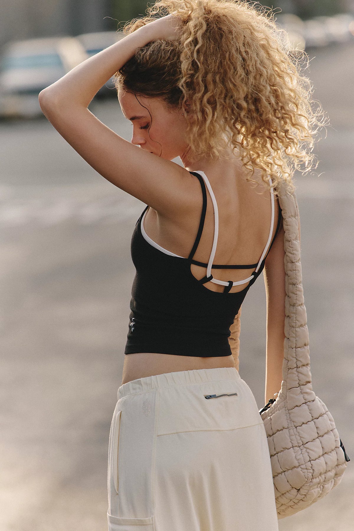 Woman in black crop top and white pants with a beige handbag on a blurred street background