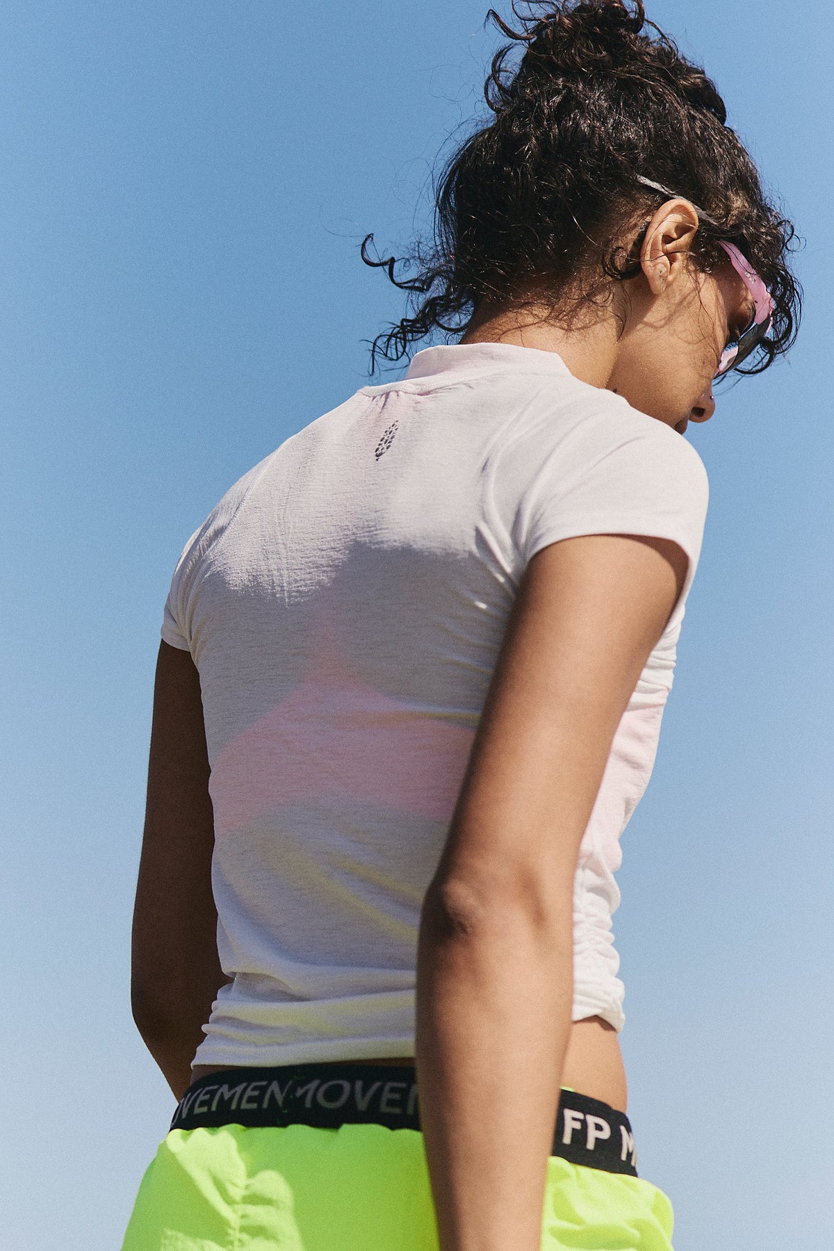 Person wearing a white athletic shirt and green shorts against a clear blue sky