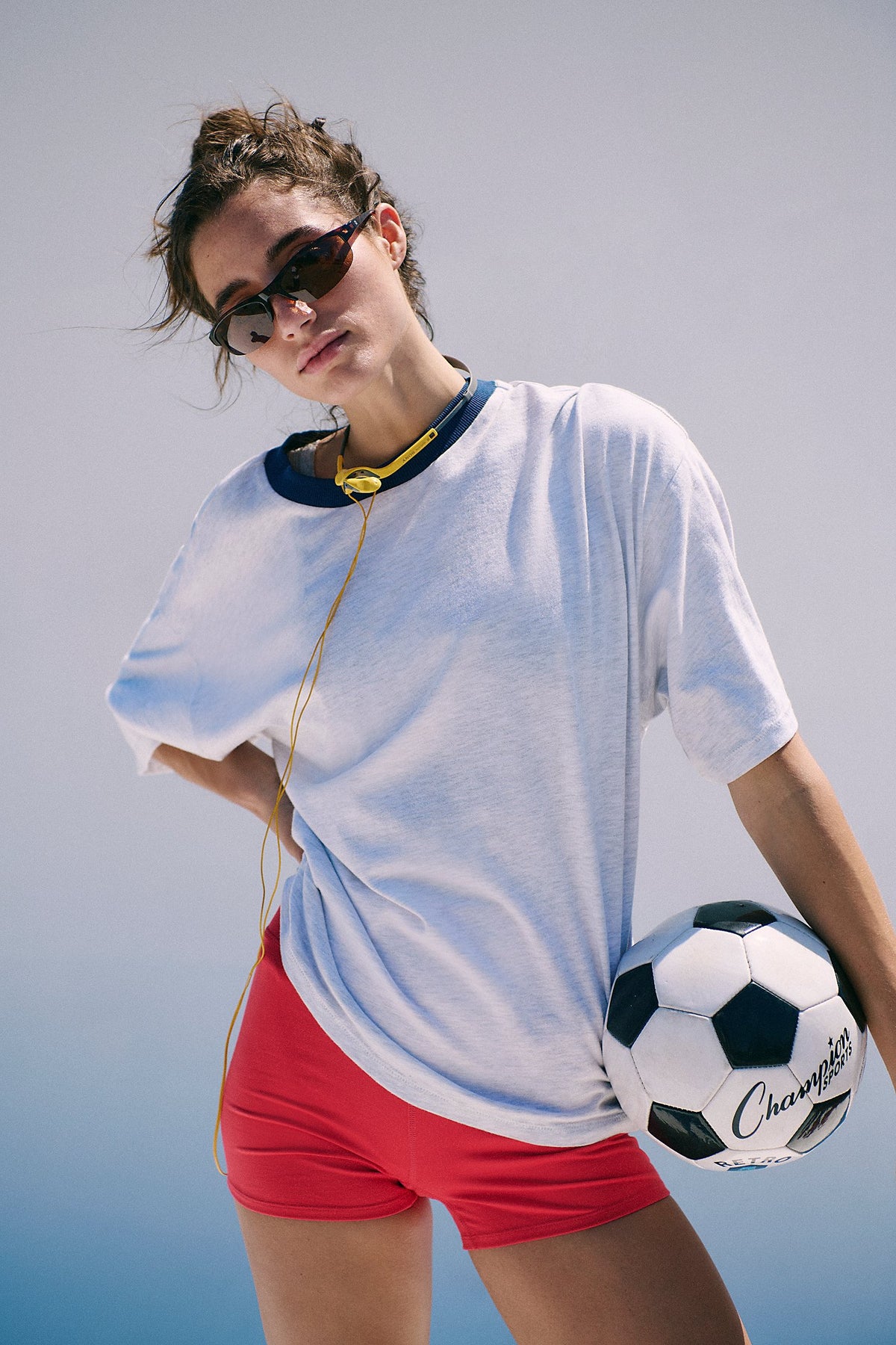 Person wearing a white shirt and red shorts holding a soccer ball against a light blue background