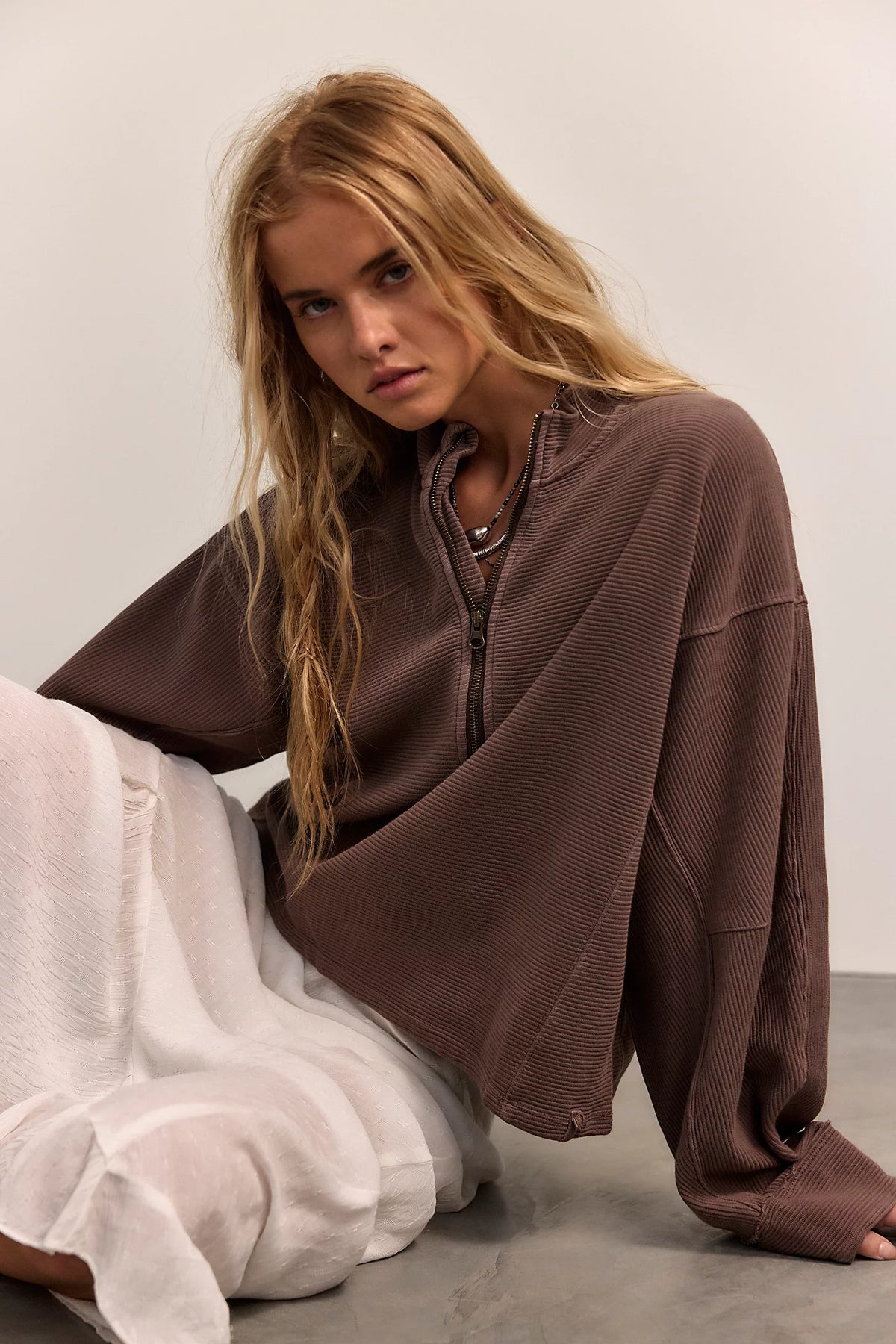 Woman wearing a brown oversized sweater over a white dress on a plain background