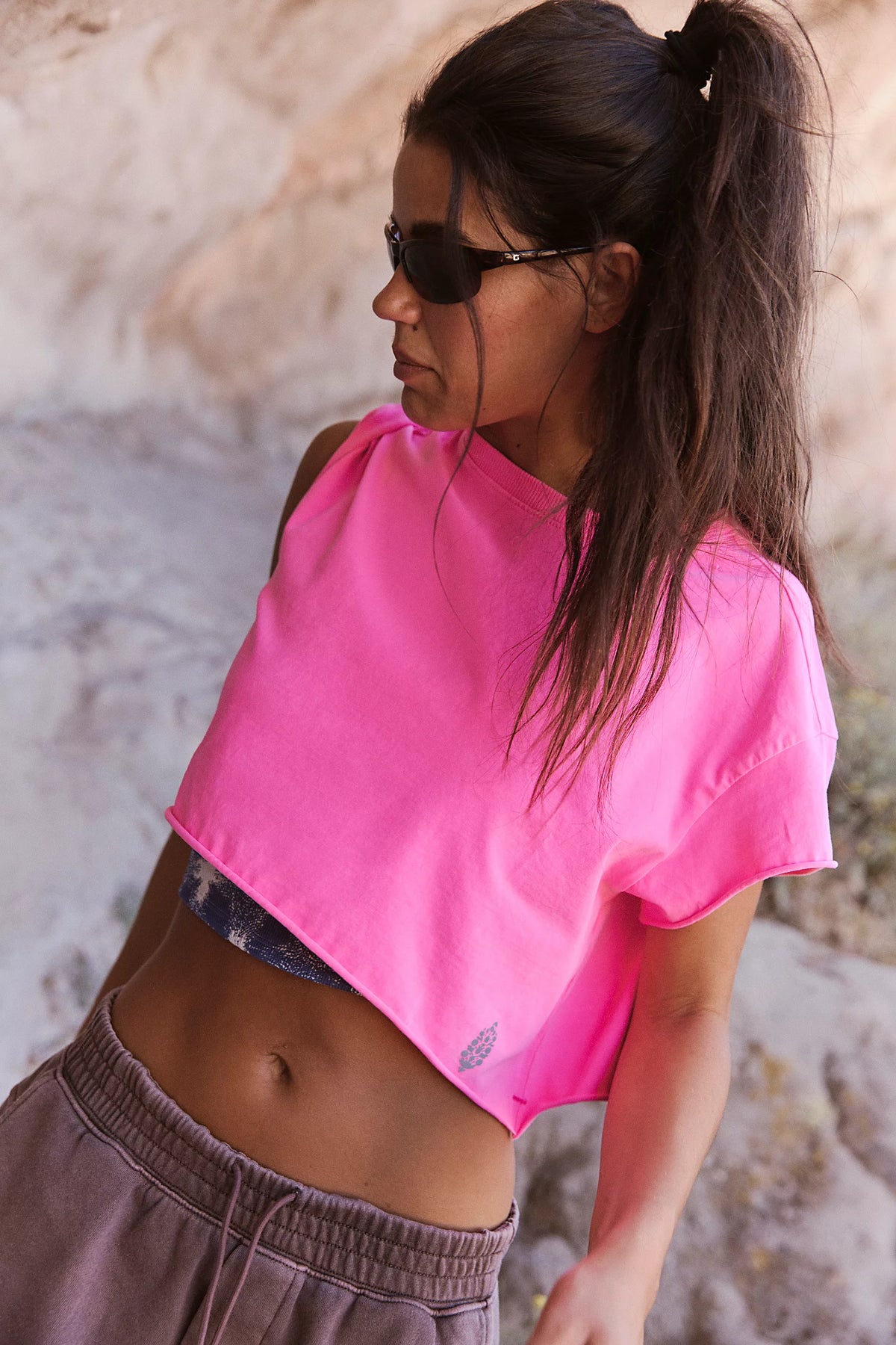 Woman wearing a bright pink crop top and sunglasses against a textured wall.