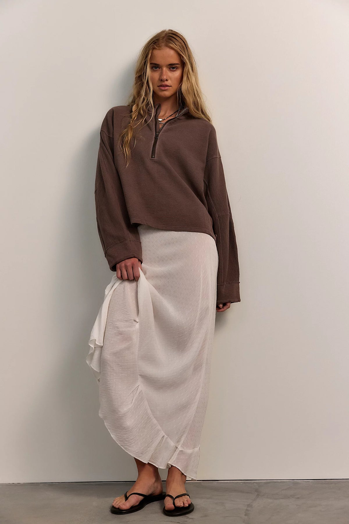 Woman wearing a brown top and white skirt against a plain wall