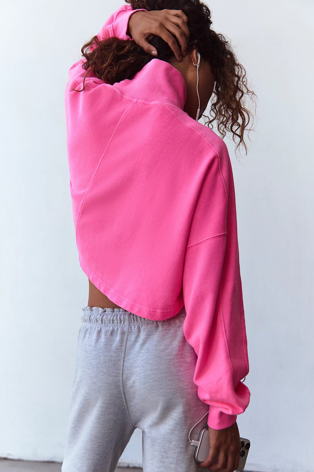 A person shown from the back wearing a bright pink cropped sweatshirt and light gray sweatpants against a plain white wall.