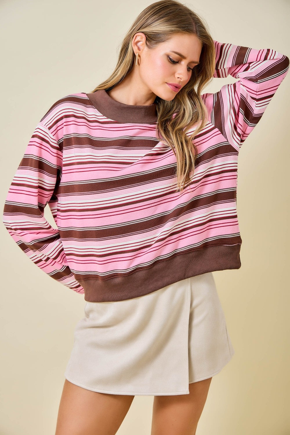 Woman wearing a pink and brown striped sweater with a beige background