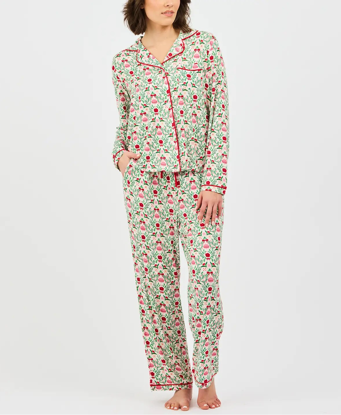A woman modeling a two-piece pajama set with a green, pink, and red floral pattern on a light background, standing against a light gray studio backdrop.