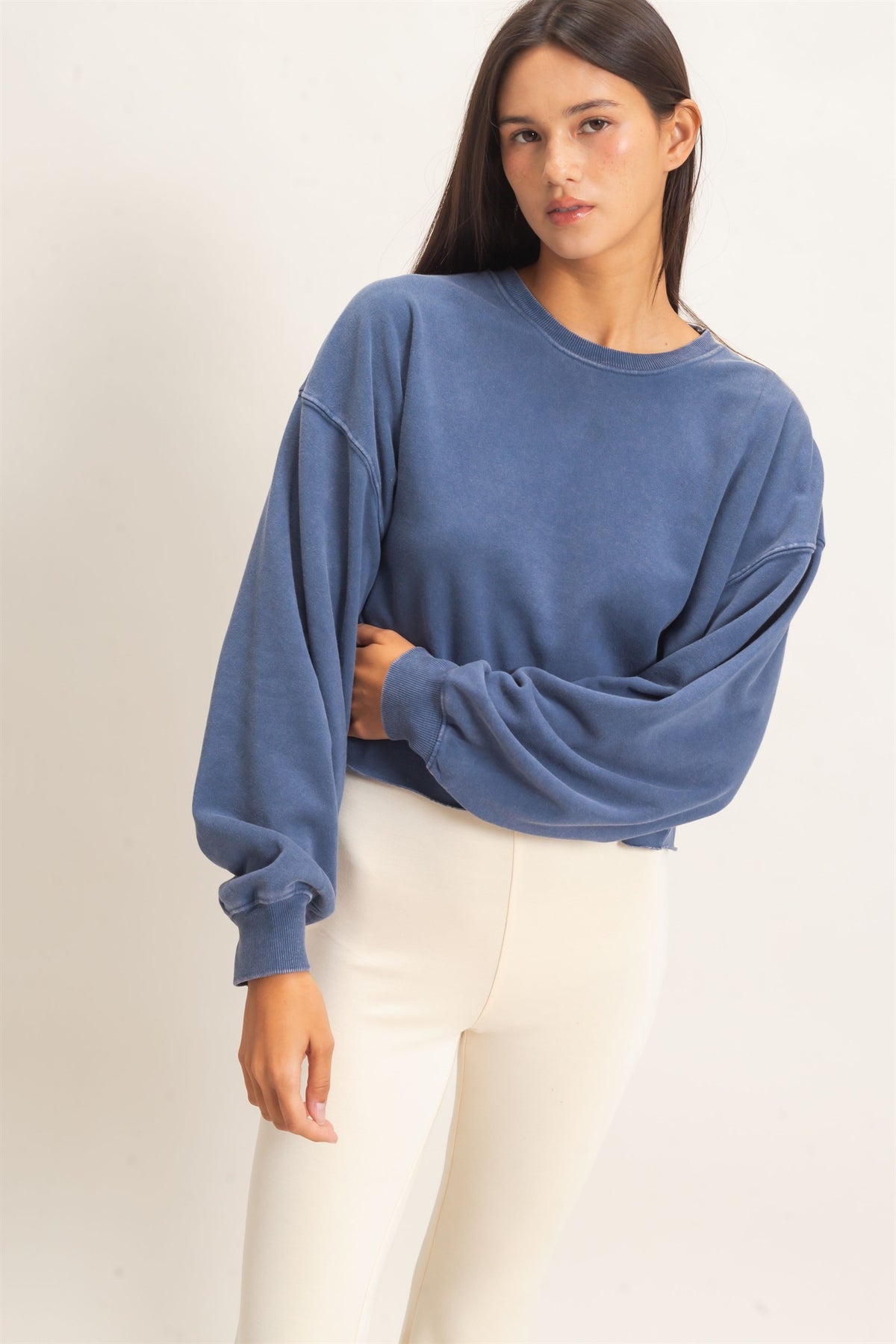 Woman wearing a blue sweater and white pants against a plain background