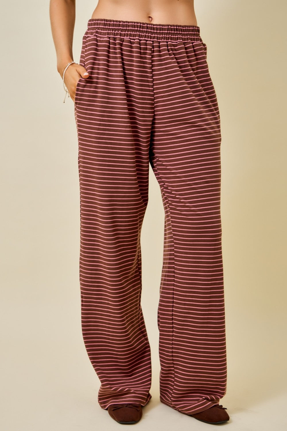 A person wearing loose, wide-leg pants with horizontal burgundy and white stripes, standing against a plain beige studio background.