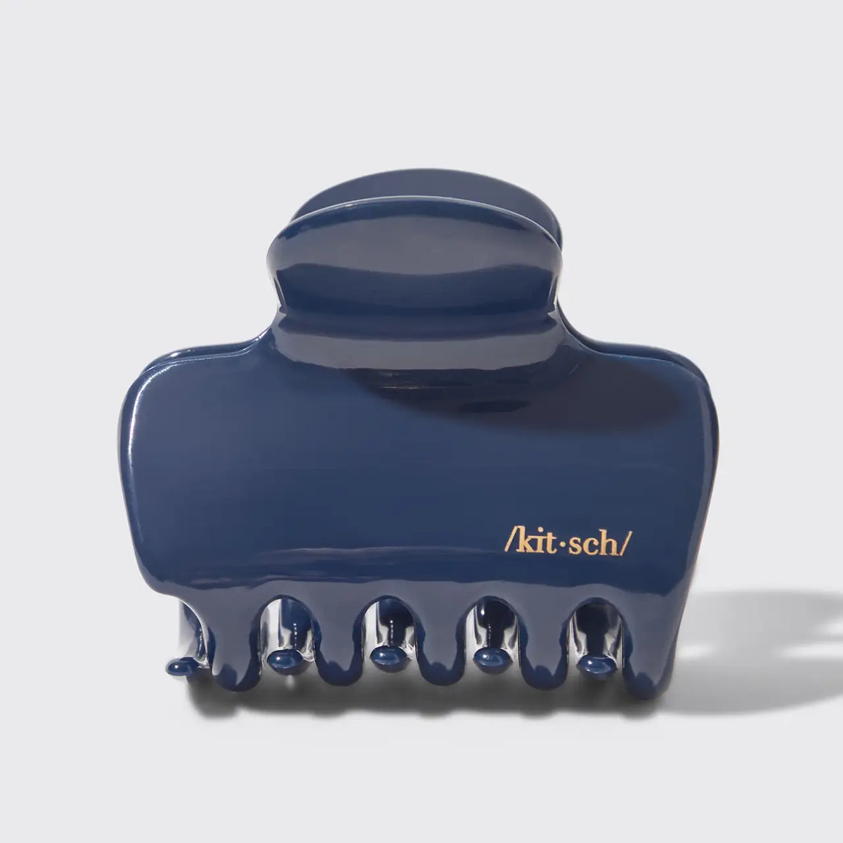 A glossy dark blue hair claw clip with gold text reading '/kit-sch/' on the front, photographed on a light gray background.