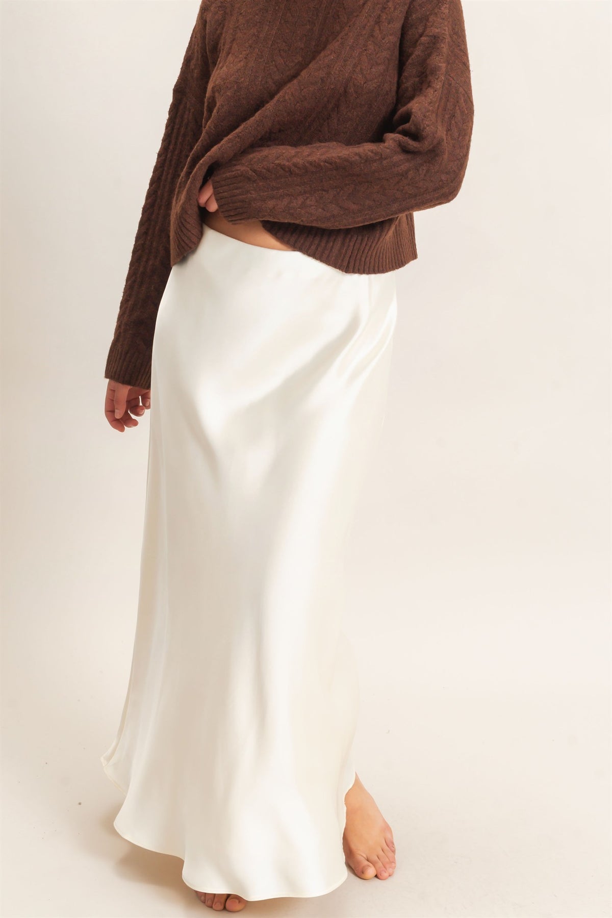 Person wearing a brown sweater and white skirt on a plain background