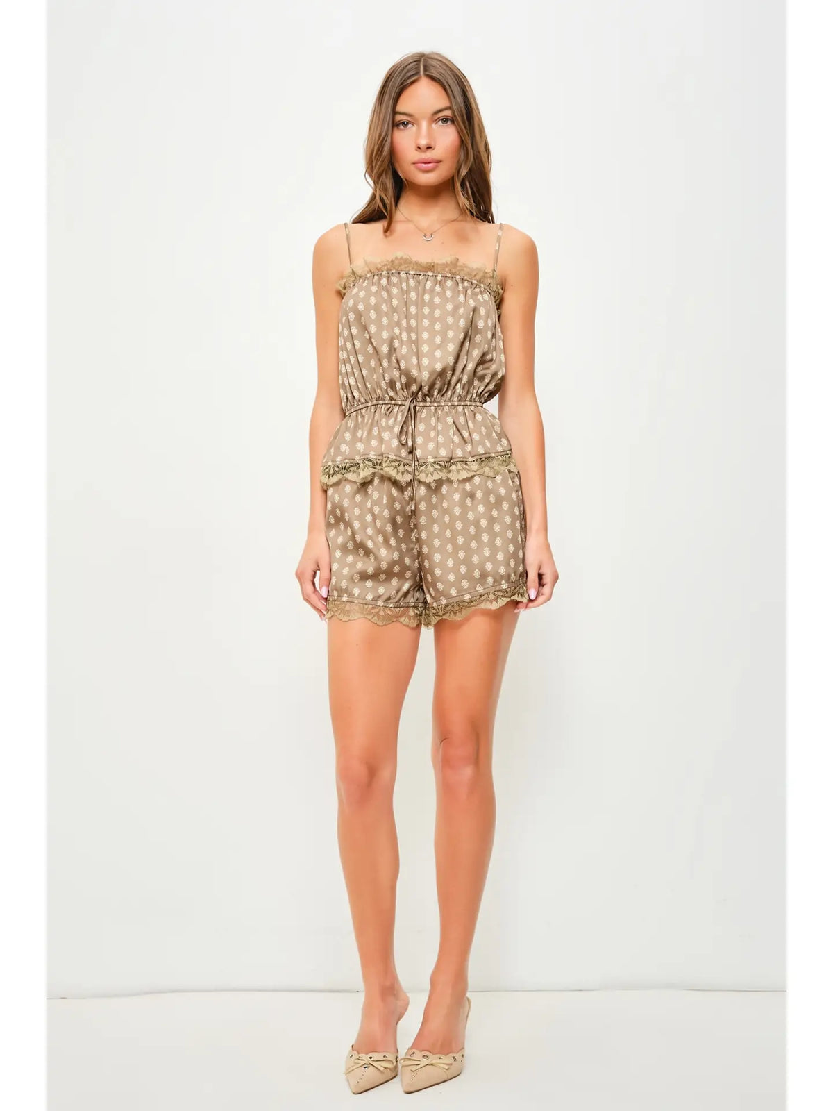 A woman modeling a beige and white polka dot romper with ruffle trim, standing against a plain white studio background.