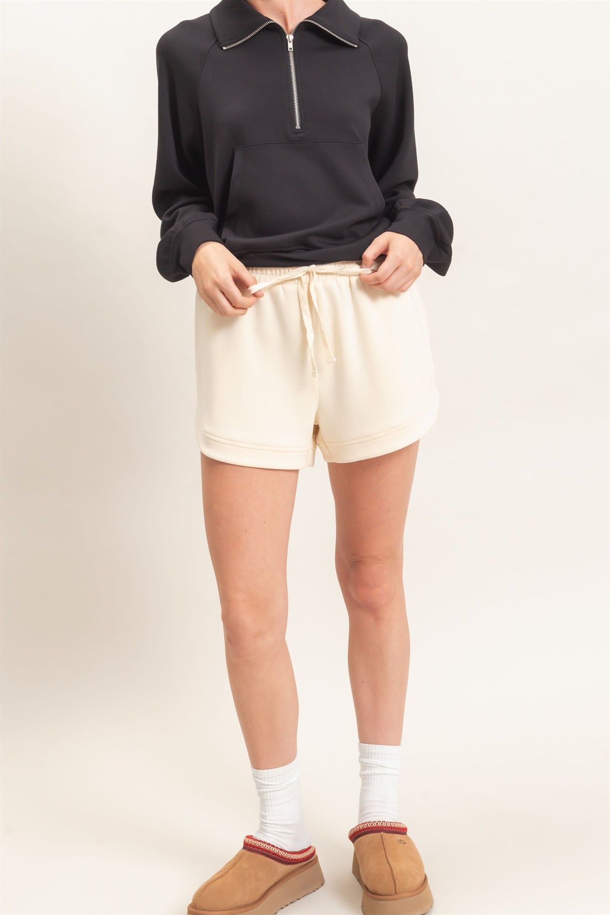 Person wearing a black sweater, cream shorts, and brown shoes on a white background