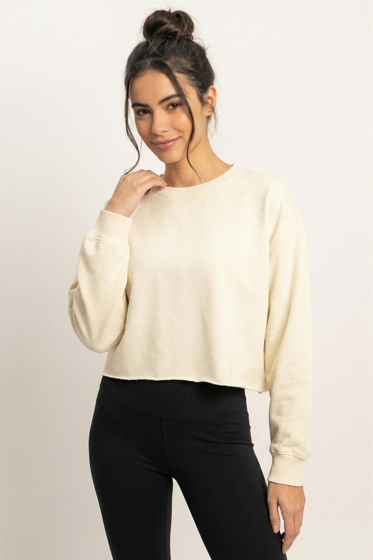 Woman wearing a cream sweater and black pants against a plain background