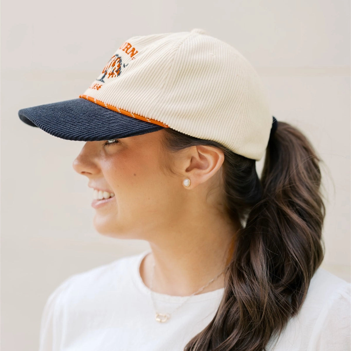 Woman wearing a beige and navy cap with a logo, smiling against a plain background