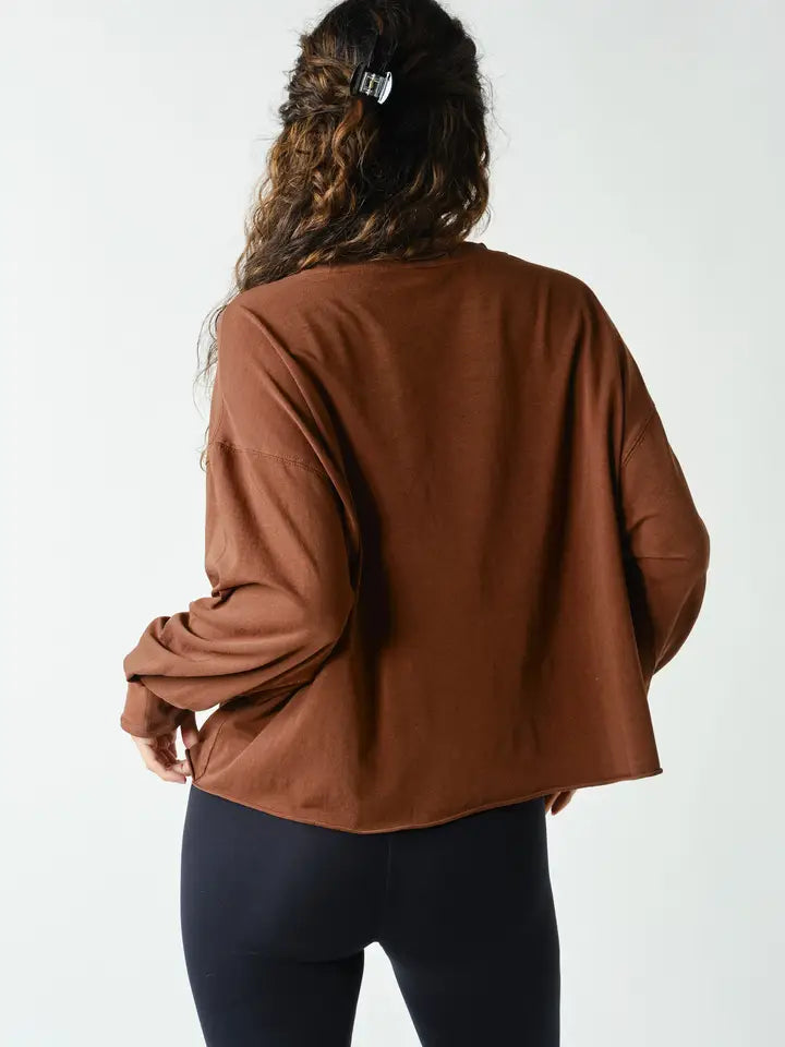 A woman viewed from behind wearing a brown long-sleeve cropped top and black leggings against a plain white background.