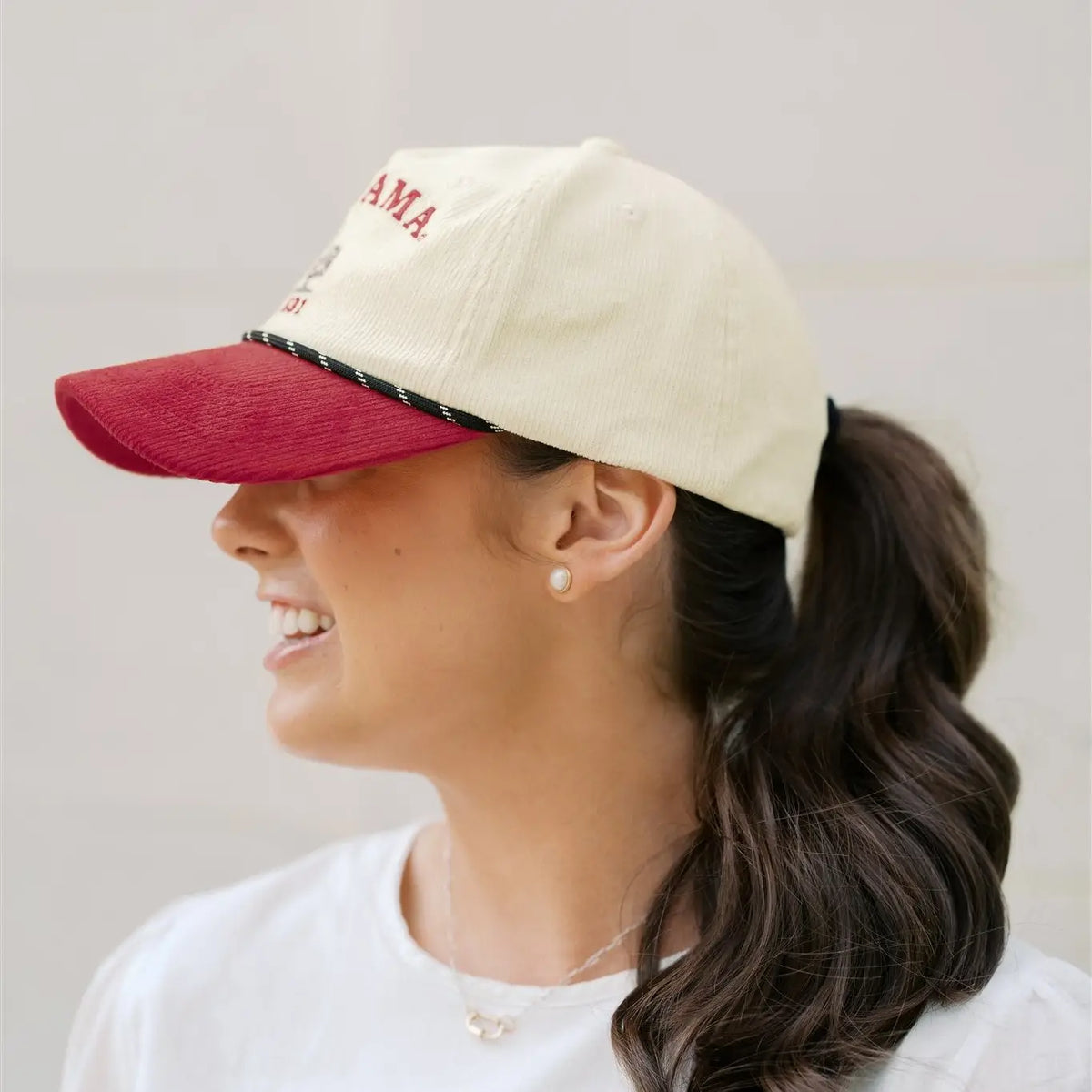 Woman wearing a beige and red cap with 'AMA' text on a plain background