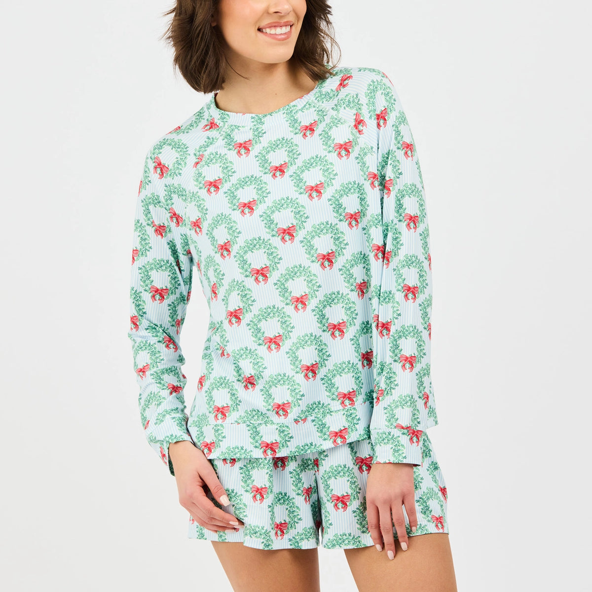 Woman wearing a festive pajama set with wreath and bow pattern on a white background