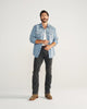 Man wearing Long sleeve denim pearl snap and gray jeans with boots on a white background