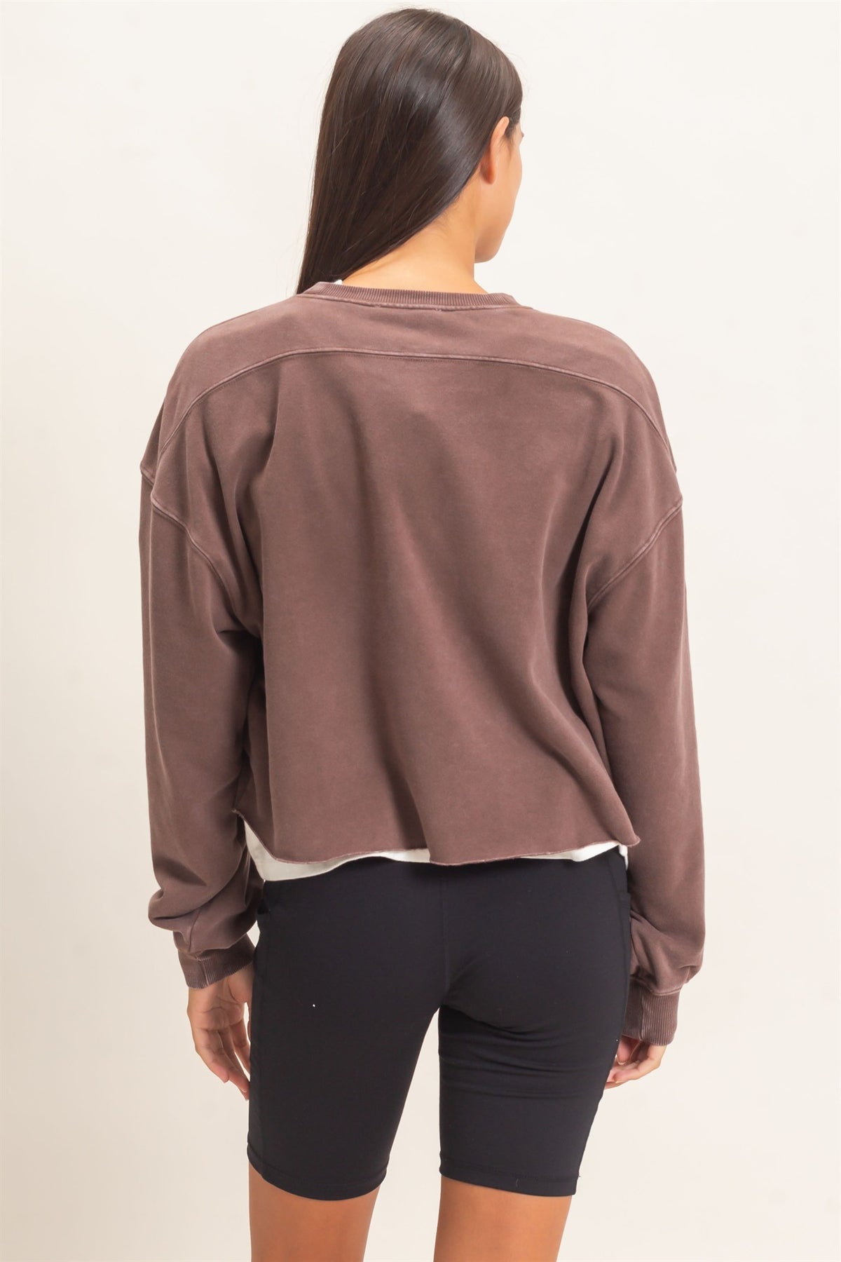 Person wearing a brown long-sleeve shirt and black shorts on a plain background