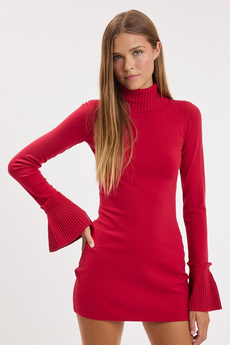 A woman modeling a bright red ribbed knit mini dress with long flared sleeves and a mock neck, set against a plain light gray studio background.