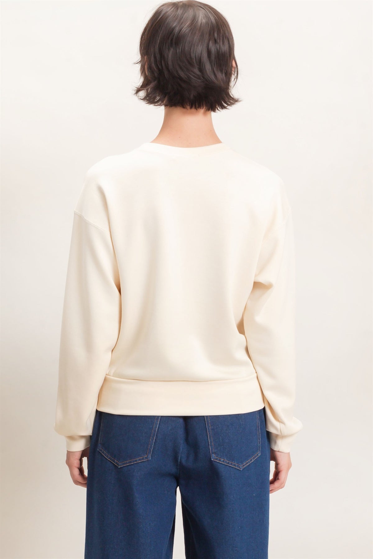 Person wearing a cream sweater and blue jeans on a plain background