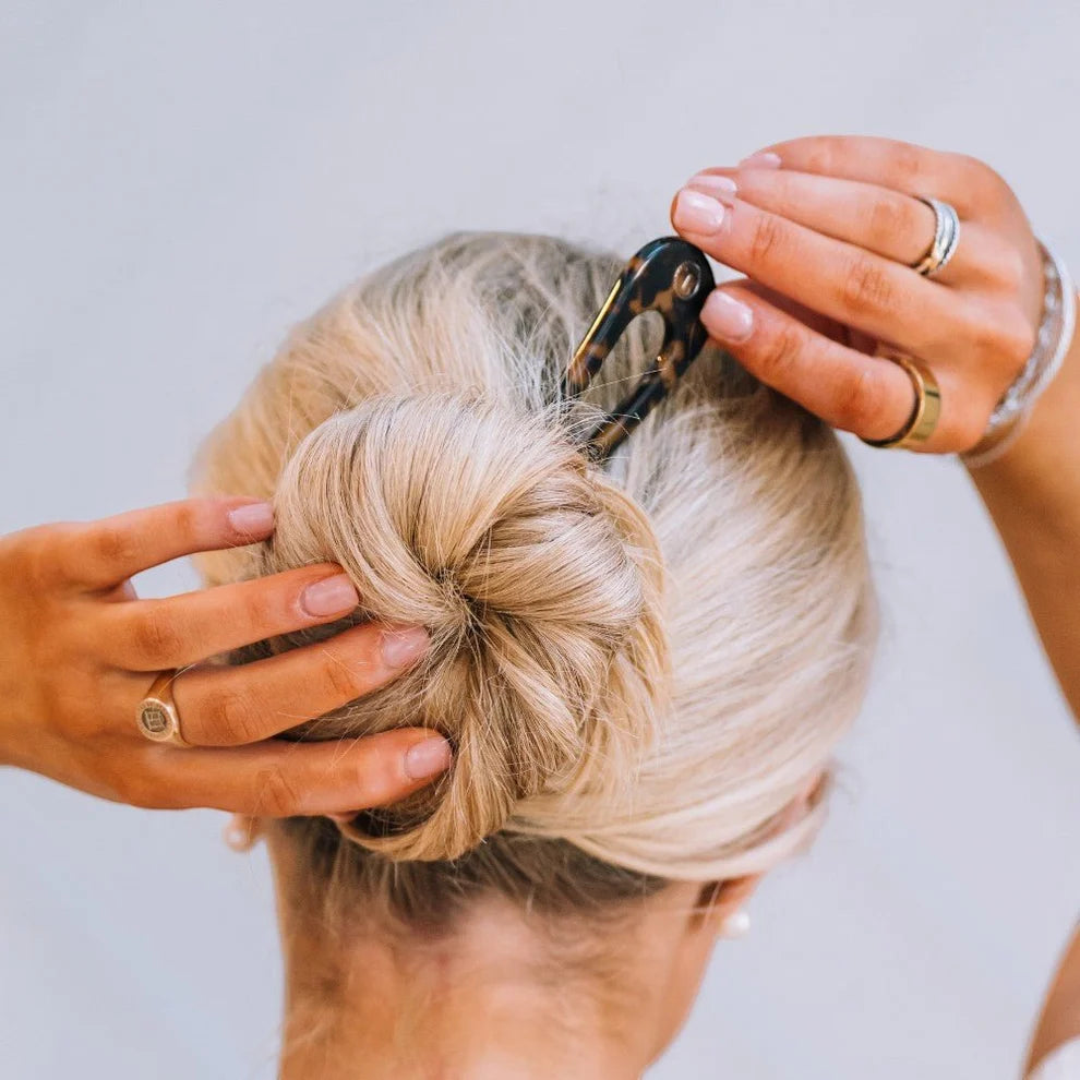 Person styling a blonde bun with a hair clip against a neutral background