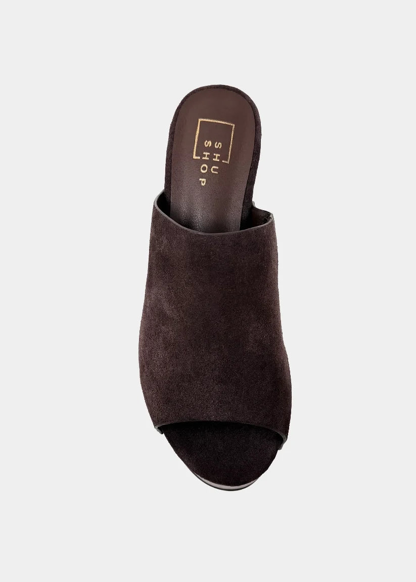A dark brown suede mule sandal with an open toe, shown from a top-down view on a light gray background. The insole features a gold square logo.