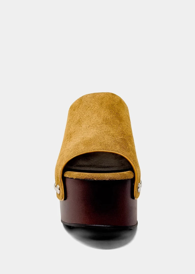 A single platform mule sandal shown from a rear three-quarter view, featuring a mustard yellow suede upper and a dark brown platform sole with a black outsole, set against a light gray background.