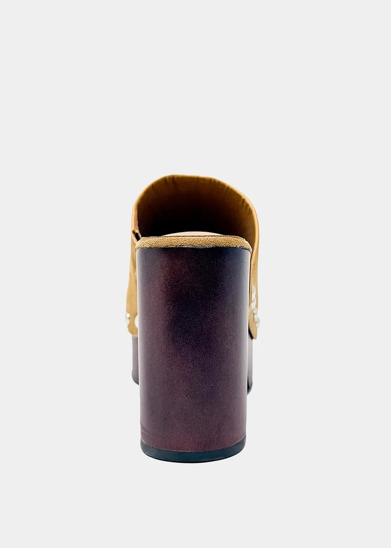 A single women's mule boot shown from the back, featuring a dark brown block heel and a tan suede collar, photographed against a light gray background.