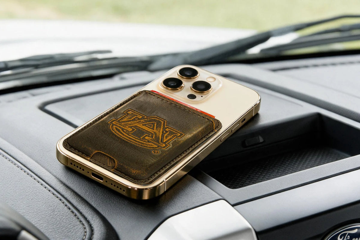 A gold-framed smartphone case with a dark brown leather back and an Auburn Tigers logo, resting on a car dashboard.