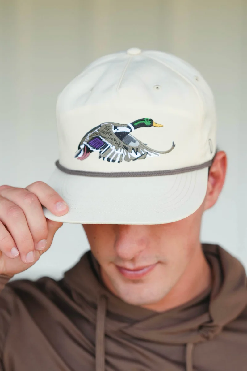 Man wearing a light gray snapback hat with an embroidered flying duck logo.