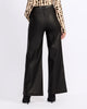 Rear view of a model wearing black wide-leg faux leather pants, a leopard-print long-sleeve top, and black heels against a plain white studio background.