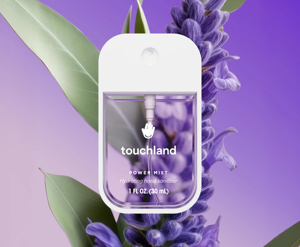 Touchland power mist bottle surrounded by lavender flowers and leaves on a purple background