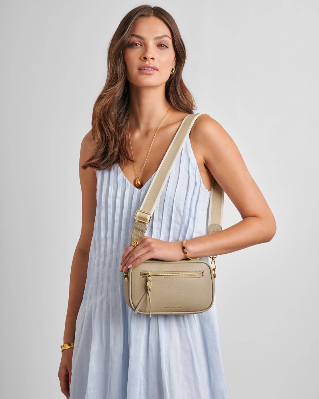 Woman wearing a light blue dress and beige crossbody bag on a plain background